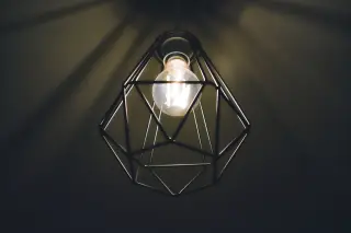 Ilustrasi: Lampu bohlam menyala di dalam kap gantung geometris berlatar belakang gelap.