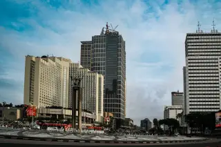 Ilustrasi: Pemandangan Bundaran HI di Jakarta dengan gedung pencakar langit dan monumen di bawah langit biru berawan.
