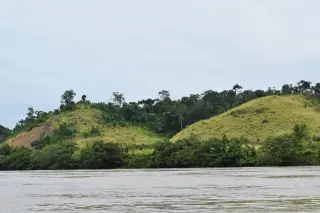 Ilustrasi: Sungai berair tenang dengan latar perbukitan hijau berumput dan pepohonan di bawah langit berawan.
