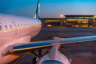 Ilustrasi: Pesawat komersial terparkir di apron bandara saat senja dengan latar terminal bercahaya.