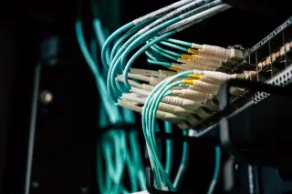 Ilustrasi: Kabel jaringan serat optik berwarna toska terpasang rapi pada rak server data center.