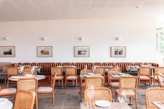 Ilustrasi: Interior restoran modern dengan deretan meja makan, kursi rotan, dan sofa panjang.