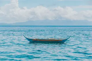 Ilustrasi: Perahu kayu tradisional mengapung di atas laut berlatar langit berawan.