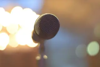 Ilustrasi: Sebuah mikrofon dari jarak dekat dengan latar belakang lampu bokeh yang kabur.