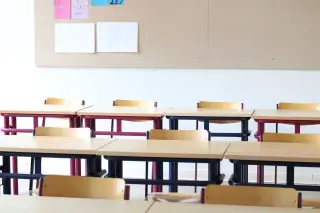 Ilustrasi: Deretan meja dan kursi kayu yang kosong di dalam ruang kelas dengan papan informasi di dinding.