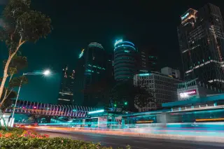 Ilustrasi: Pemandangan malam jalan raya kota dengan gedung bertingkat dan jejak cahaya kendaraan.