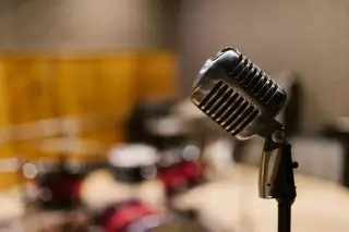 Ilustrasi: Mikrofon antik di studio musik dengan latar belakang set drum yang buram.