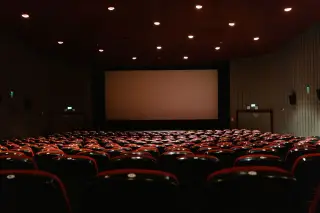 Ilustrasi: Deretan kursi bioskop kosong menghadap layar lebar dalam ruangan bercahaya temaram.