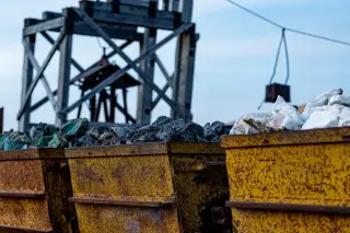 Ilustrasi: Gerobak tambang berkarat berisi bebatuan mineral di dekat struktur kayu penambangan.