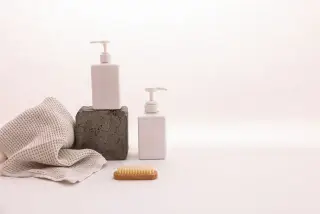 Ilustrasi: Dua botol pompa putih polos bersama kain dan sikat kecil dengan latar belakang putih.