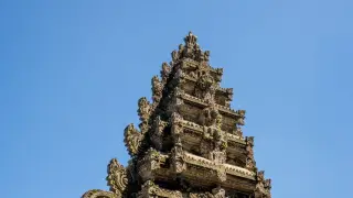 Ilustrasi: Puncak candi atau gapura berukir khas Bali dengan latar belakang langit biru cerah.
