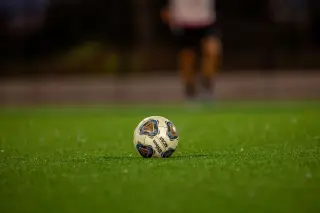 Ilustrasi: Sebuah bola sepak di atas rumput hijau dengan latar belakang seseorang yang buram.