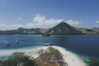 Ilustrasi: Pemandangan pesisir pantai pasir putih dengan perahu wisata dan perbukitan di kawasan Labuan Bajo.
