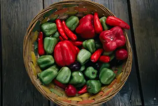 Ilustrasi: Keranjang anyaman berisi cabai dan paprika merah serta hijau di atas permukaan kayu.