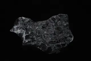 Ilustrasi: Bongkahan batu mineral gelap berkilau dengan latar belakang hitam pekat.
