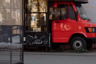 Ilustrasi: Sebuah truk makanan berwarna merah terparkir di area luar ruangan dengan papan menu bertuliskan pizza.