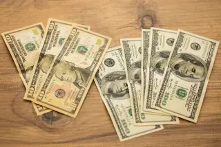 Ilustrasi: Beberapa lembar uang kertas dolar AS tersebar di atas meja kayu.