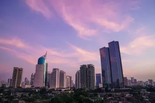 Ilustrasi: Pemandangan gedung-gedung pencakar langit Jakarta di bawah langit senja berwarna merah muda.