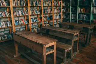 Ilustrasi: Ruang kelas bernuansa pedesaan dengan deretan meja kayu dan rak penuh buku.