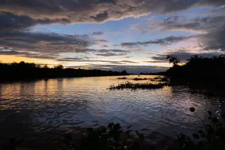 Ilustrasi: Pemandangan sungai bertenang saat senja dengan pantulan langit berawan di permukaan air.