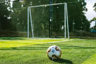 Ilustrasi: Sebuah bola sepak di lapangan rumput dengan latar gawang dan pepohonan.