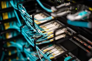 Ilustrasi: Deretan kabel jaringan optik biru terhubung ke panel server pusat data.