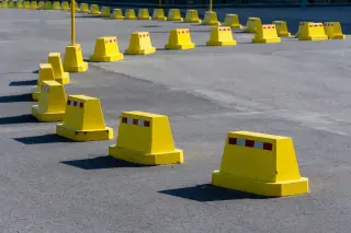 Ilustrasi: Deretan pembatas jalan berwarna kuning tersusun melengkung di atas permukaan aspal.