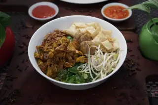 Ilustrasi: Semangkuk mie ayam dengan bakso, tauge, kerupuk pangsit, dan saus sambal di atas meja.