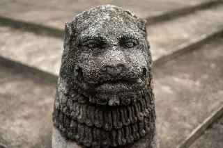 Ilustrasi: Patung singa batu kuno berlumut dengan latar belakang tangga batu.