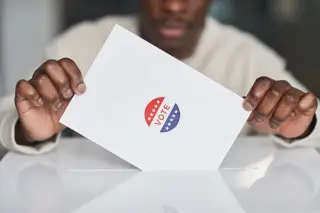 Ilustrasi: Seseorang memasukkan surat suara bertuliskan 'vote' ke dalam celah kotak suara putih.
