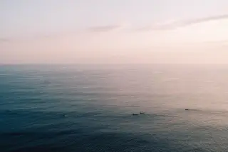 Ilustrasi: Pemandangan laut luas yang tenang di pagi hari dengan beberapa perahu kecil di kejauhan.