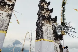 Ilustrasi: Gerbang candi bentar Bali dengan latar pemandangan gunung dan awan.