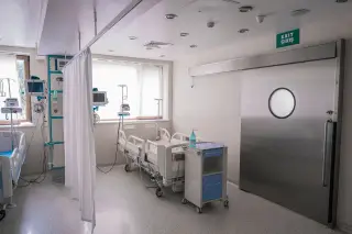 Ilustrasi: Kamar rawat inap rumah sakit berisi ranjang medis kosong, peralatan monitor, dan pintu geser metalik.