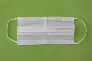 Ilustrasi: Sebuah masker medis putih terbentang di atas latar belakang hijau polos.