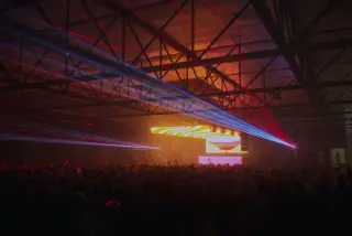 Ilustrasi: Sorotan lampu laser warna-warni di atas kerumunan penonton konser musik dalam ruangan.