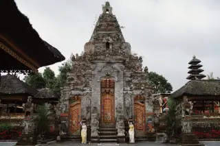 Ilustrasi: Bangunan gerbang pura tradisional khas Bali dengan ukiran batu dan patung di depannya.