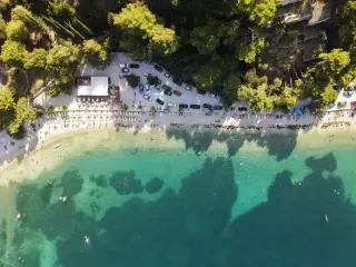 Ilustrasi: Pemandangan udara area parkir mobil dan pengunjung di tepi pantai berair jernih.