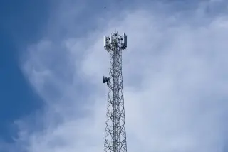 Ilustrasi: Menara pemancar telekomunikasi berdiri tegak dengan latar belakang langit biru berawan tipis.