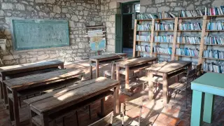 Ilustrasi: Ruang kelas kuno kosong dengan deretan meja kayu, papan tulis, dan rak buku besar.