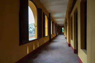 Ilustrasi: Lorong panjang sebuah bangunan bergaya kolonial yang sepi dengan lantai ubin dan jendela berjejer.