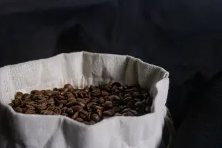 Ilustrasi: Biji kopi sangrai di dalam kantong kain berlatar belakang gelap.