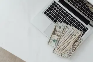 Ilustrasi: Tumpukan uang kertas dolar AS tergeletak di atas papan ketik laptop putih.
