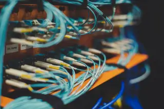 Ilustrasi: Deretan kabel serat optik berwarna biru yang terhubung pada panel server jaringan.