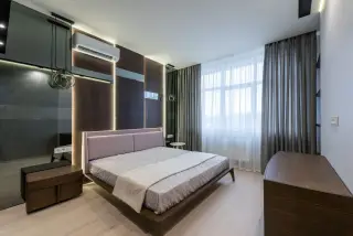 Ilustrasi: Interior kamar tidur modern dengan ranjang tertata rapi, tirai jendela, dan pendingin ruangan.