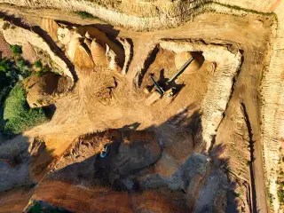 Ilustrasi: Pemandangan udara area tambang terbuka dengan tumpukan material tanah dan alat berat.