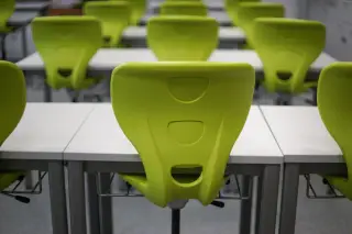 Ilustrasi: Deretan kursi plastik hijau terang dan meja putih di dalam ruang kelas kosong.