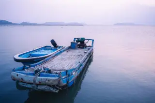 Ilustrasi: Dua perahu kayu biru bersandar di perairan tenang saat senja.