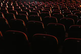 Ilustrasi: Deretan kursi bioskop berwarna merah dalam ruangan yang gelap berpenerangan minim.