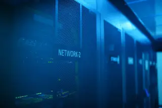 Ilustrasi: Deretan rak server pusat data dengan lampu indikator berlatar cahaya biru.