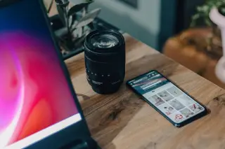 Ilustrasi: Sebuah lensa kamera dan ponsel pintar tergeletak di atas meja kayu di dekat laptop.